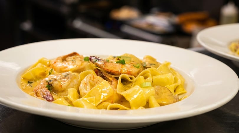 Close-up of shrimp and pasta in a creamy sauce, garnished with green onions, in a white bowl.