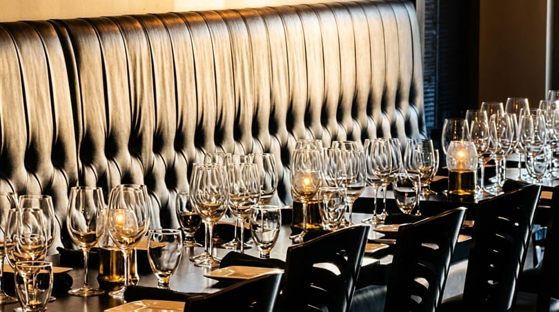 Elegantly set dining table with wine glasses, plates, and candles, against a tufted leather booth.