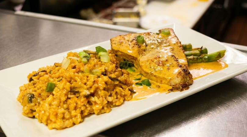 A plate of salmon with creamy sauce, risotto, and asparagus on a white rectangular plate.